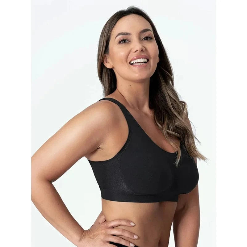 A woman with long wavy brown hair smiles while wearing a black seamless sports bra against a plain white background.