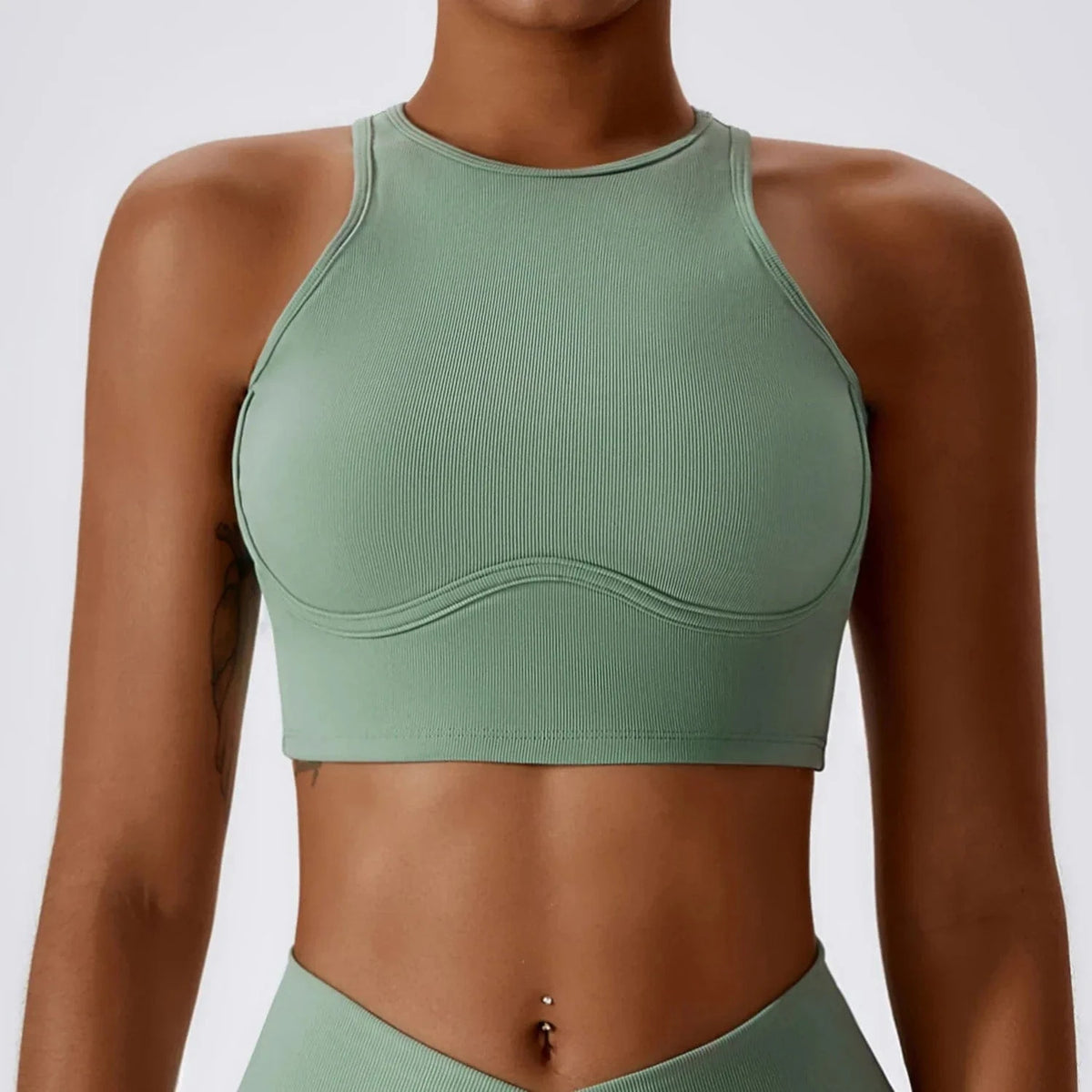 A sage green ribbed cropped tank top with a high neckline and a contoured seam under the bust worn by a person.