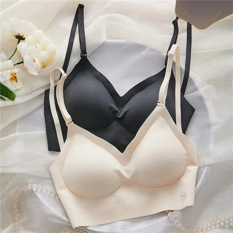 Two seamless, wireless bras in beige and black are layered on a white fabric surface next to a small branch of white flowers.