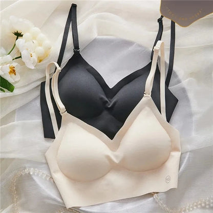 Two seamless, wireless bras in beige and black are layered on a white fabric surface next to a small branch of white flowers.