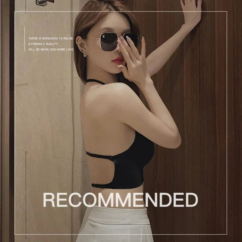 A woman wearing a black backless crop top stands against a wooden wall while wearing large sunglasses.