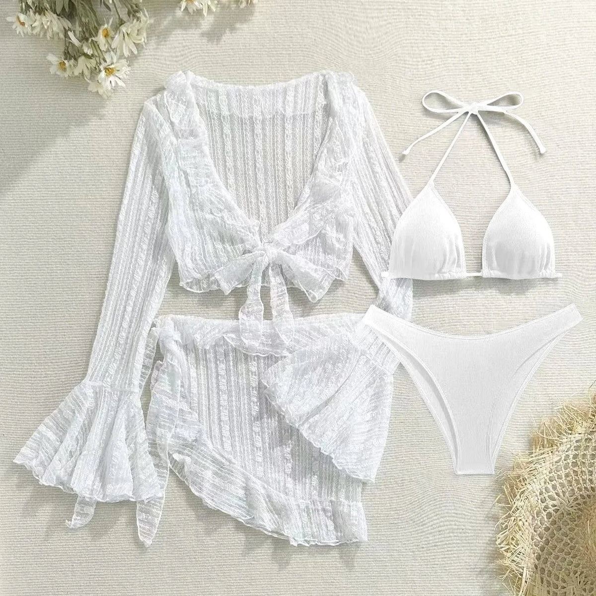 A white three-piece set featuring a bikini top, bikini bottoms, and a matching sheer long-sleeved tie-front cover-up with ruffled cuffs and a matching ruffle skirt, arranged on a textured beige surface.