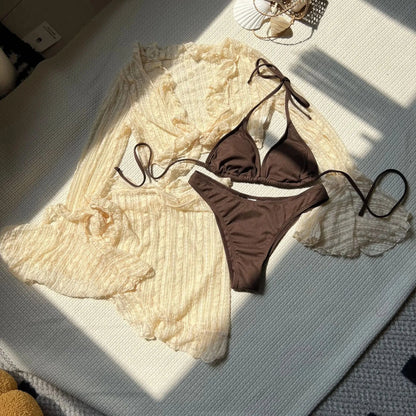 A dark brown bikini set is displayed next to a sheer, light cream-colored long-sleeve cover-up with ruffled edges on a white textured surface.