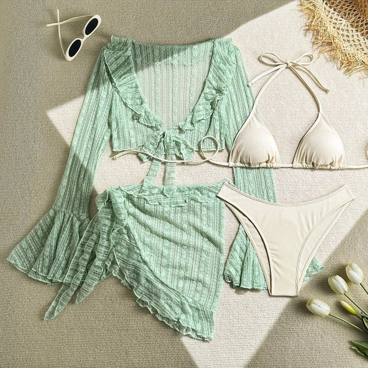A beige string bikini set consisting of a triangle top and high-cut bottoms, accompanied by a matching sage green sheer ruffled long-sleeve crop top and a wrap-style ruffled mini skirt, displayed on a textured surface with sunglasses and tu