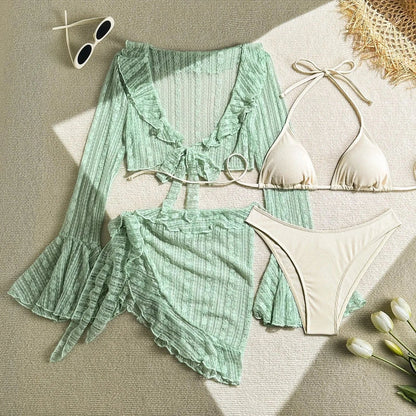 A beige string bikini set consisting of a triangle top and high-cut bottoms, accompanied by a matching sage green sheer ruffled long-sleeve crop top and a wrap-style ruffled mini skirt, displayed on a textured surface with sunglasses and tu
