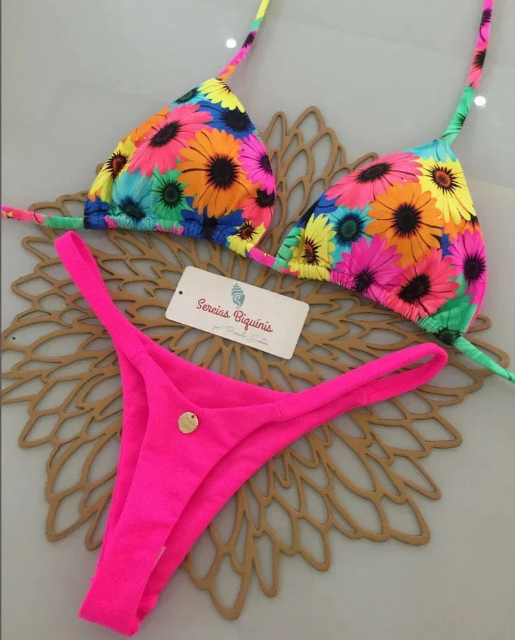 A bikini set featuring a neon pink bottom and a triangle top with a colorful floral pattern on a light-colored surface.