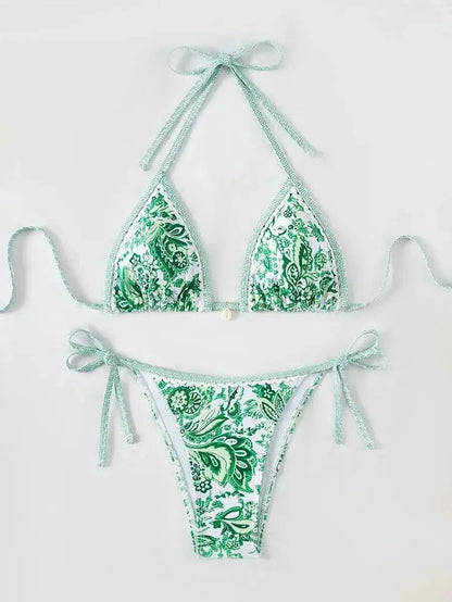 A two-piece bikini set featuring a green and white paisley pattern with decorative trim and side-tie detailing on the bottoms.