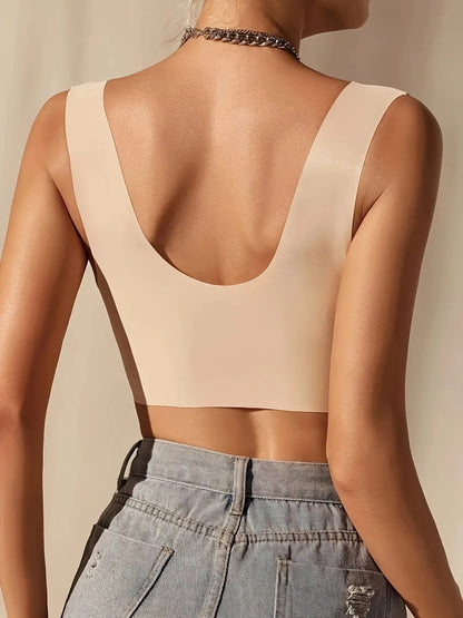 A beige seamless scoop-back crop top worn by a person from behind, paired with blue denim jeans.