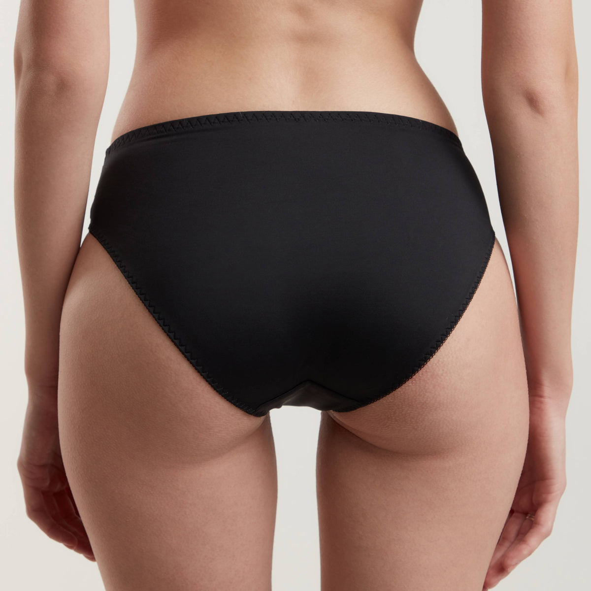 A pair of black bikini-style underwear viewed from the back on a person against a neutral background.