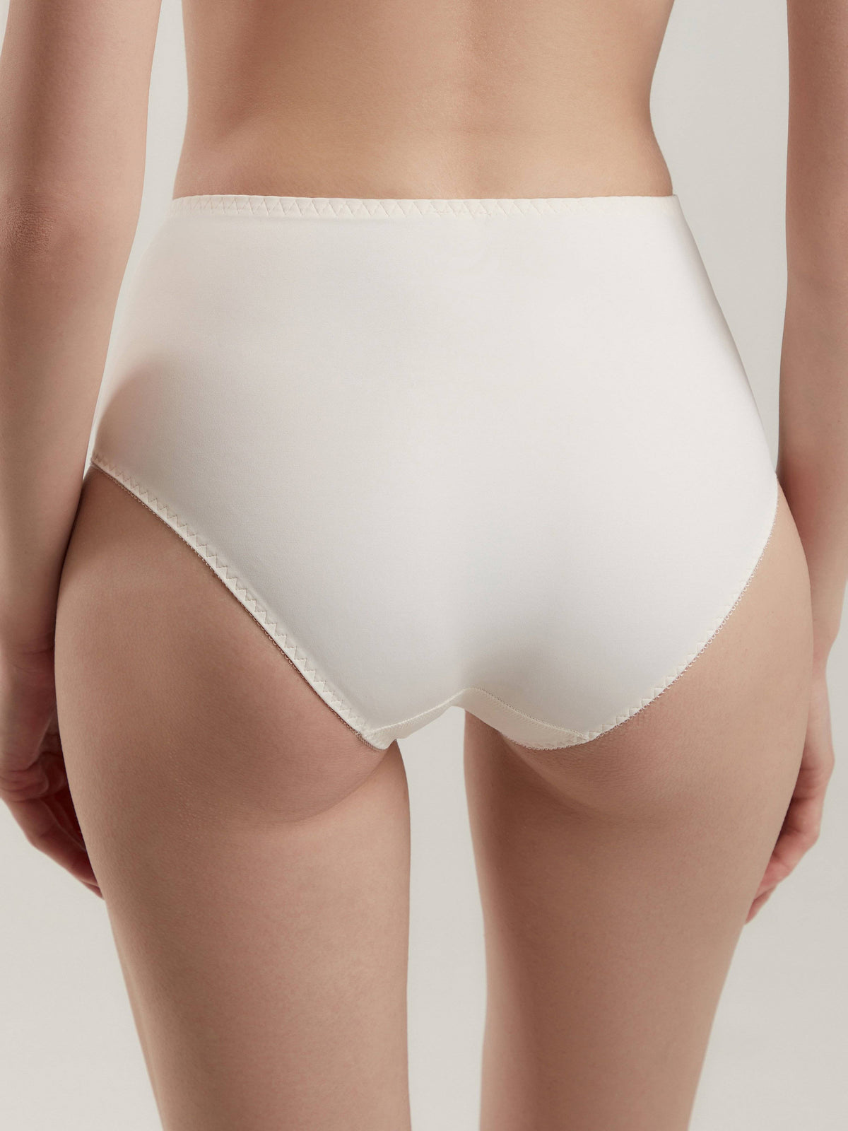 White high-waisted briefs seen from the back, featuring a simple seamless design with delicate scalloped trim along the leg openings and waistband.