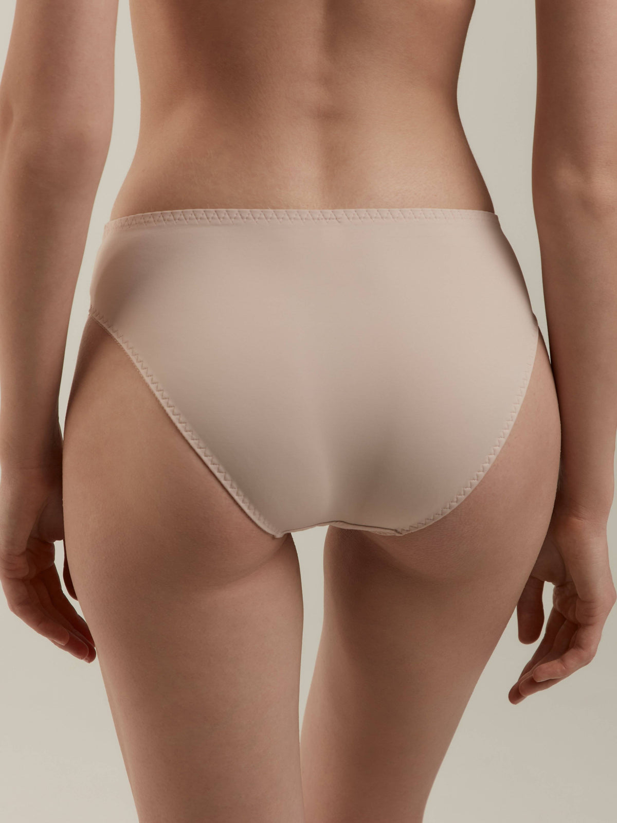 A pair of nude-colored, high-cut briefs viewed from the back on a person with a neutral background.