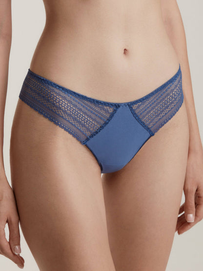 A woman wearing blue lace-trimmed thong underwear against a plain light background.