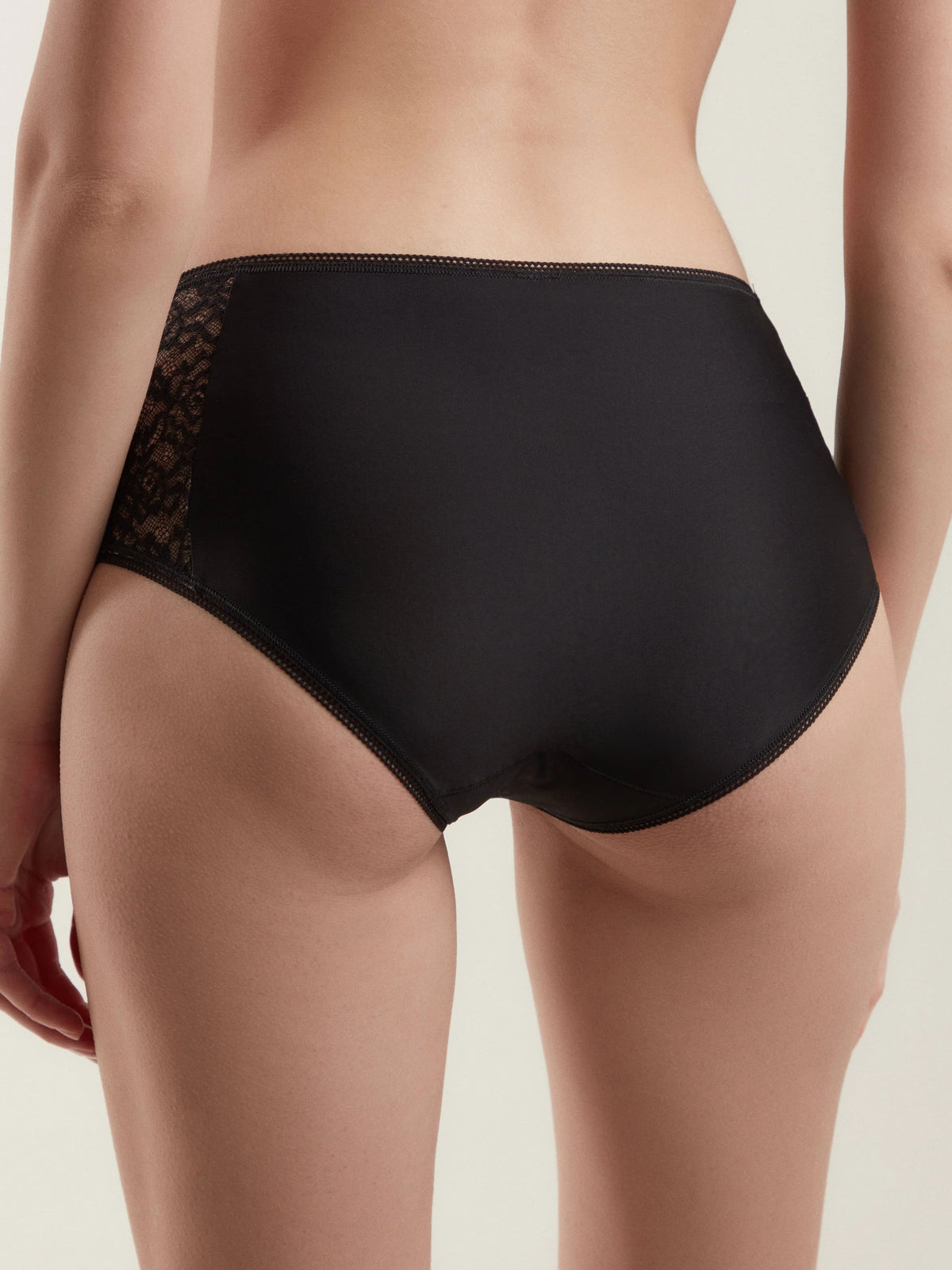 Black full-coverage briefs worn on a person, featuring smooth fabric on the back and delicate lace side panels.