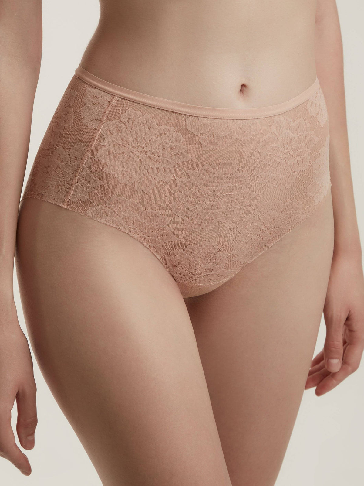 A pair of high-waisted briefs in a nude beige color, featuring an all-over floral lace pattern and smooth elastic trim at the waist and leg openings.