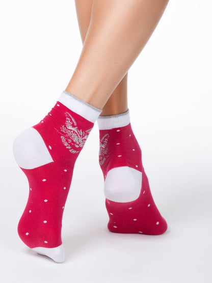 A pair of red ankle socks featuring a silver cat design and small white polka dots, worn on a person's feet against a white background.