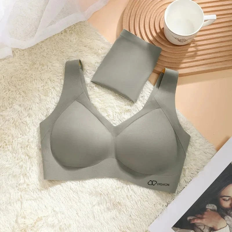 A sage green seamless bralette with wide shoulder straps and a matching folded piece of fabric, laid flat on a white faux fur rug next to a white mug and a fashion magazine.