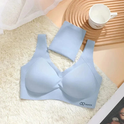 A light blue seamless bralette with a V-neckline lies on a white faux fur rug next to a matching folded garment, a white mug, and a wooden coaster.