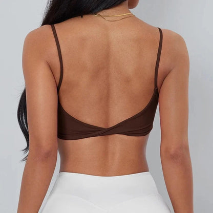 A dark brown backless crop top featuring thin shoulder straps and a twisted detail at the center back, worn by a person with white bottoms.