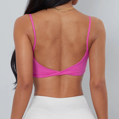 A back view of a person wearing a bright pink cropped camisole with thin straps and a twisted detail at the lower back, paired with white athletic leggings.