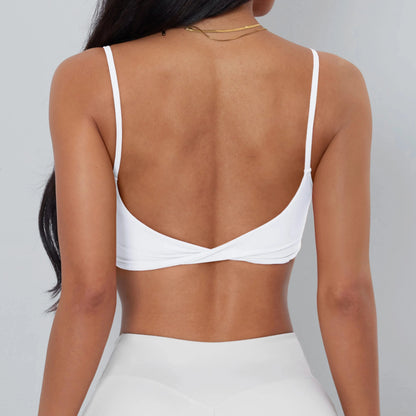 A white sports bra with spaghetti straps and a twisted detail at the center back, worn by a person against a light gray background.