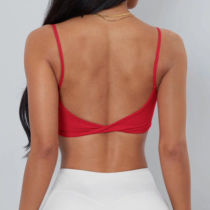 A back view of a person wearing a bright red cropped camisole top featuring thin straps and a twisted hem detail, paired with white athletic leggings.