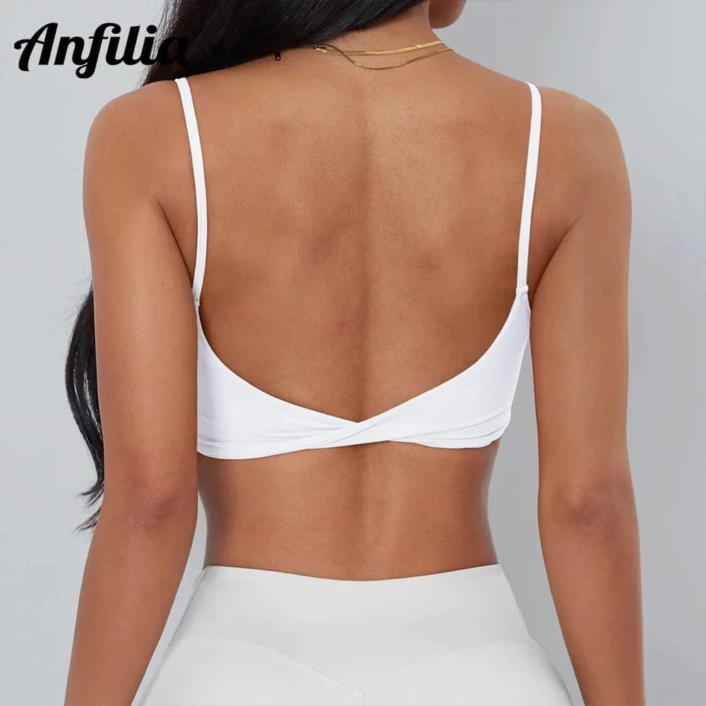 A white sports bra with thin shoulder straps and a twisted detail at the center back, worn by a person against a plain light gray background.
