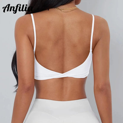 A white sports bra with thin shoulder straps and a twisted detail at the center back, worn by a person against a plain light gray background.