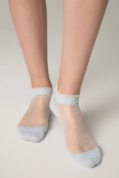 Sheer ankle socks in a shimmering light blue color feature a solid blue toe and heel with a delicate ruffled edge at the cuff, modeled on a person's feet against a neutral background.