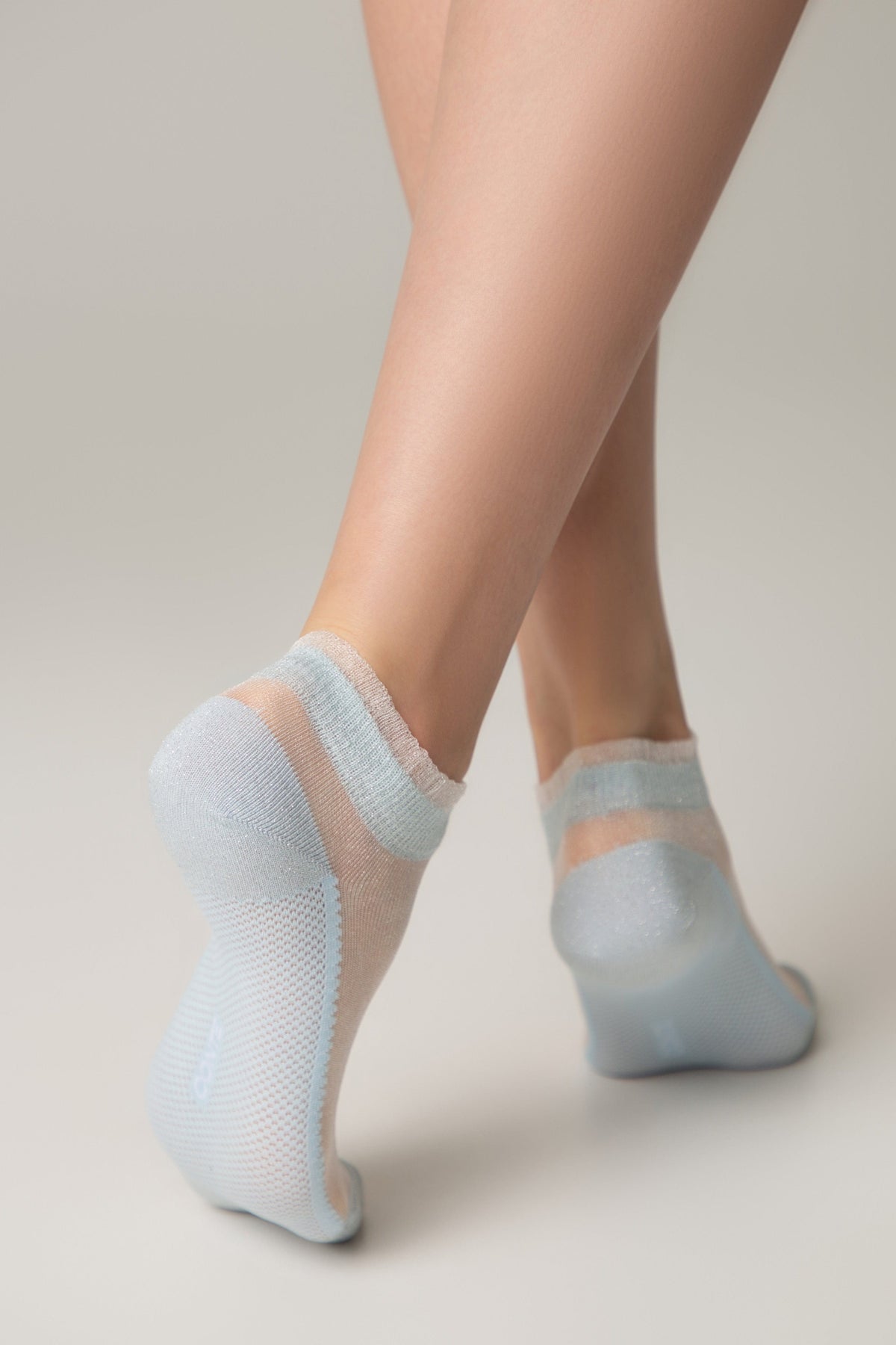 Light blue, sheer ankle socks with a textured, reinforced heel and toe, worn on a person's feet against a solid light gray background.