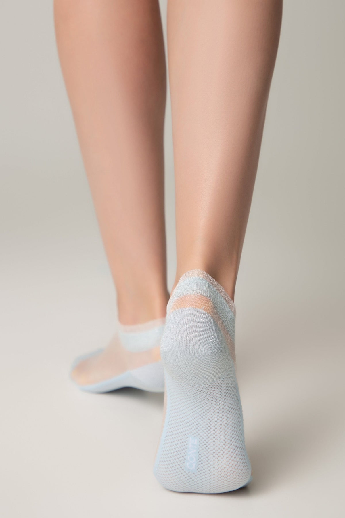 Light blue low-cut sheer ankle socks with a subtle horizontal stripe detail worn on a pair of legs against a plain light gray background.