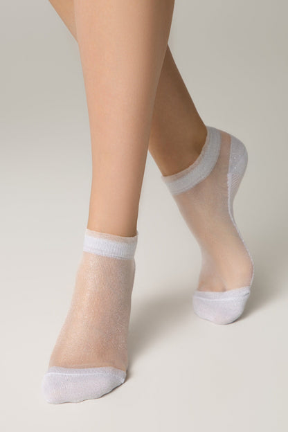 Sheer white ankle socks with a subtle shimmer worn on a pair of legs against a plain light gray background.