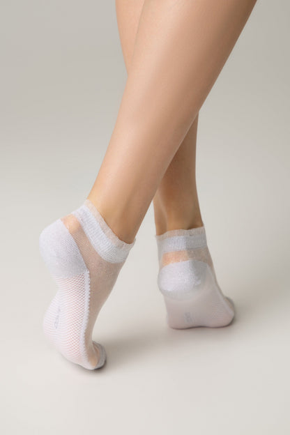 Sheer white low-cut ankle socks with a shimmering finish and reinforced toes and heels worn by a model against a neutral background.