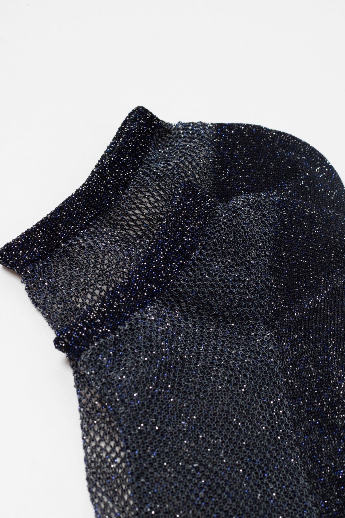 An ankle-length sock in a shimmering, dark blue and black open-knit mesh fabric.