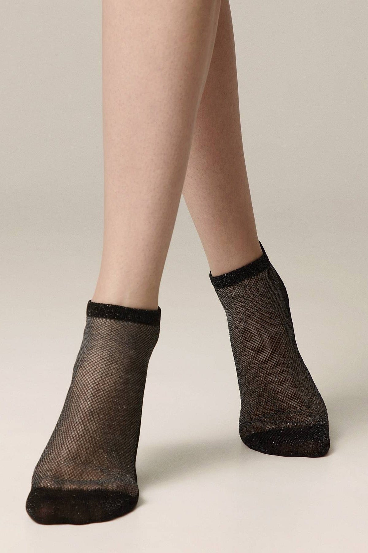 A pair of black ankle-length fishnet socks worn on a person's feet against a neutral background.