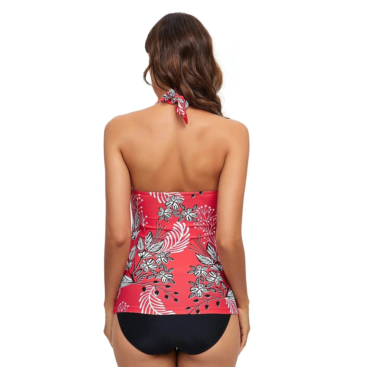 A woman stands with her back to the camera wearing a red halter-neck tankini top featuring a white and black floral print paired with solid black bikini bottoms.