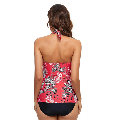 A woman stands with her back to the camera wearing a red halter-neck tankini top featuring a white and black floral print paired with solid black bikini bottoms.