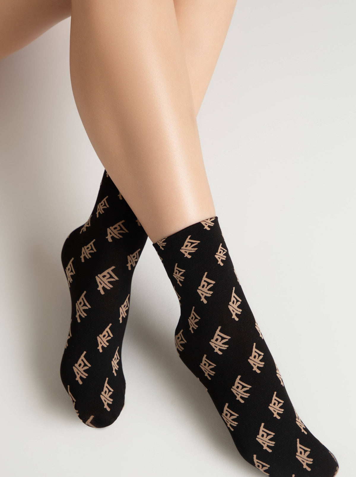 A pair of black crew-length socks featuring a repeating gold art graphic pattern worn on a person's legs against a neutral background.