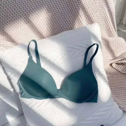 A teal-colored wireless bra with adjustable straps sits on a white textured pillow against a backdrop of soft fabric.