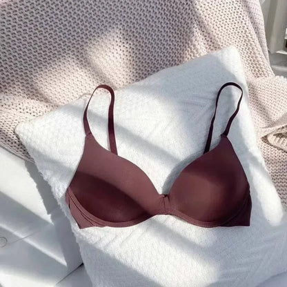 A maroon underwire bra with thin adjustable straps rests on a plush white textured cushion.