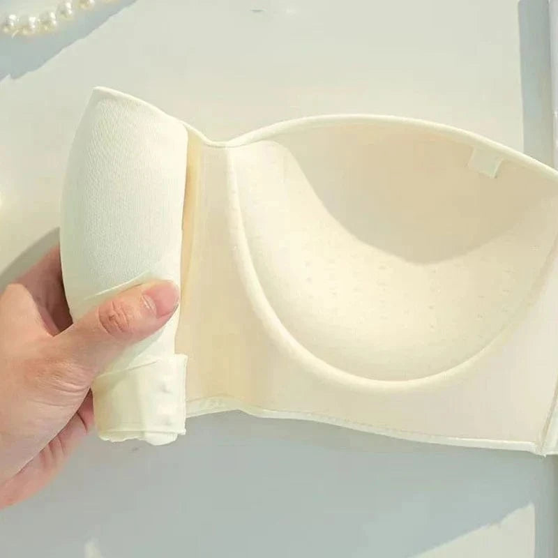 A beige strapless bra held in a hand against a white background, highlighting its molded cups and smooth seamless design.