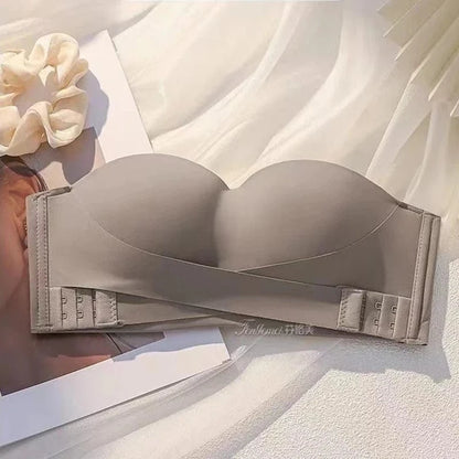 A strapless, taupe-colored, padded push-up bra featuring a unique crisscross front design and a wide back band with double hook-and-eye closures, displayed against a light, draped fabric background.