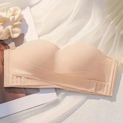 A strapless, beige, molded-cup bra features a crisscross band design with multiple hook-and-eye closures on the back, displayed against a light, draped fabric background.