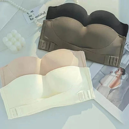 Four strapless bras in black, brown, beige, and cream are arranged on a white surface next to a decorative card and a photo.