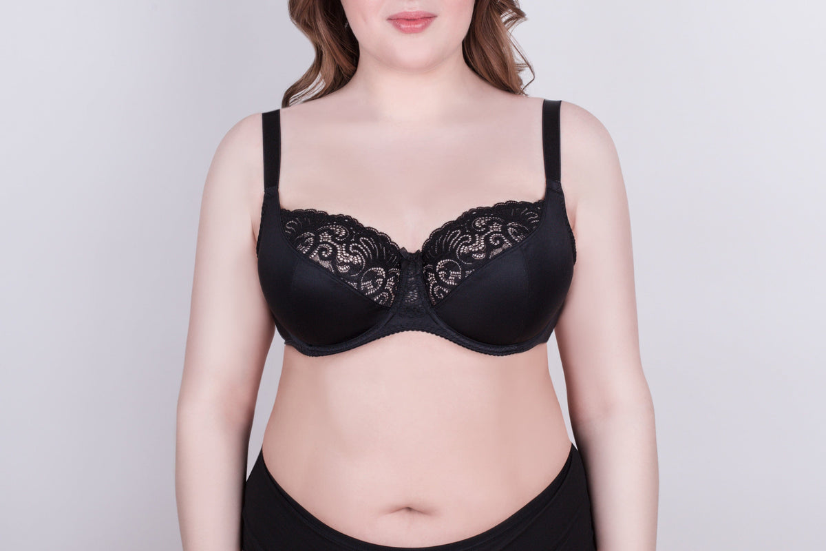 A black bra with black lace detailing on the upper cups and thick adjustable shoulder straps worn by a person against a plain light gray background.