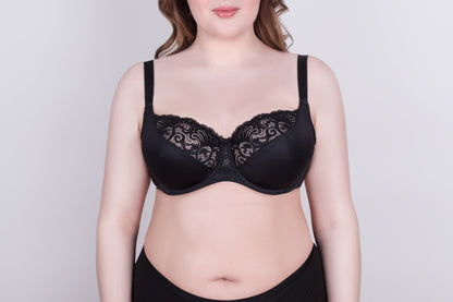 A black bra with black lace detailing on the upper cups and thick adjustable shoulder straps worn by a person against a plain light gray background.