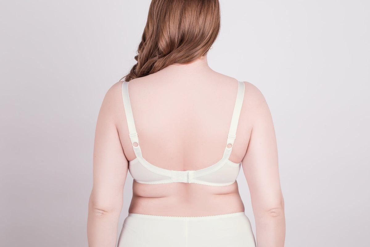 A beige bra seen from the back on a woman, featuring wide adjustable straps and a hook-and-eye closure against a light grey background.