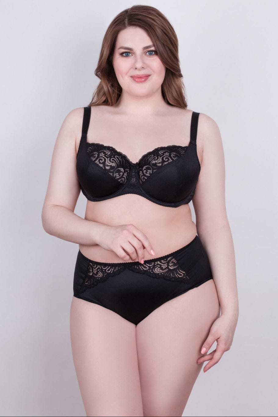 A woman models a black bra and matching high-waisted briefs featuring decorative lace detailing along the upper cups and the waistband.