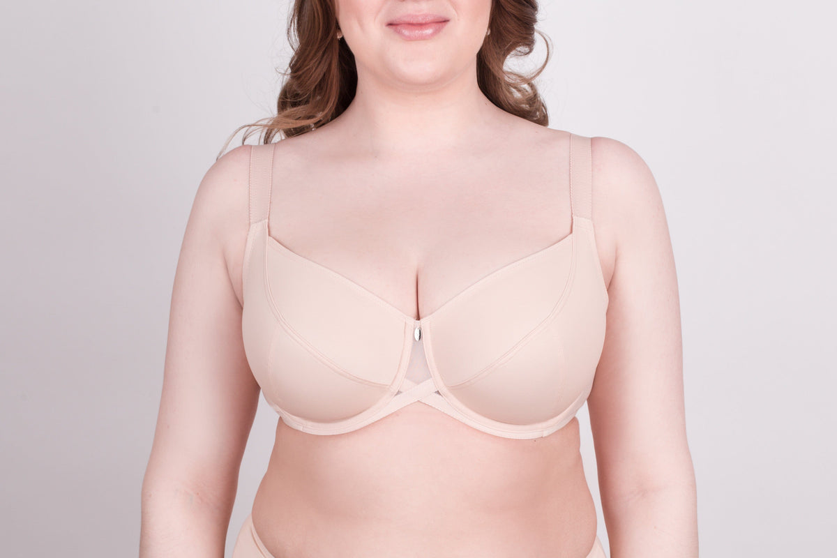 A beige full-coverage bra with a center front mesh cutout and adjustable straps worn by a woman against a light gray background.