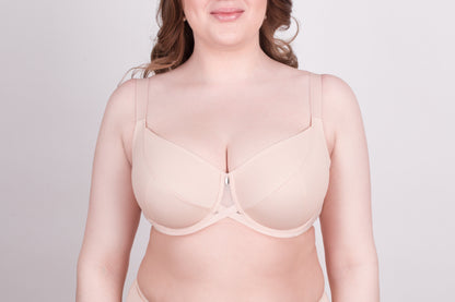 A beige full-coverage bra with a center front mesh cutout and adjustable straps worn by a woman against a light gray background.