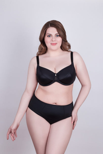 A woman wearing a black matching bra and high-waisted panty set against a plain light gray background.